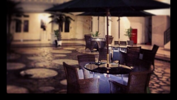 An outdoor seating area with tables and chairs, an umbrella, and potted plants. - Ramayana Hotel (Makassar)