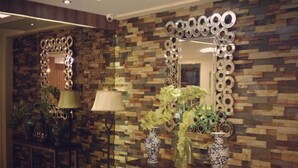 A modern interior with a stone-patterned wall, a console table with vases, a floor lamp, and a mirror with circular frames. - Ramayana Hotel (Makassar)