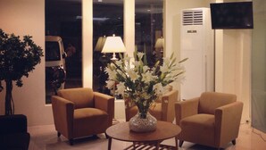 A modern living room with two armchairs, a round coffee table, and a vase of flowers. - Ramayana Hotel (Makassar)