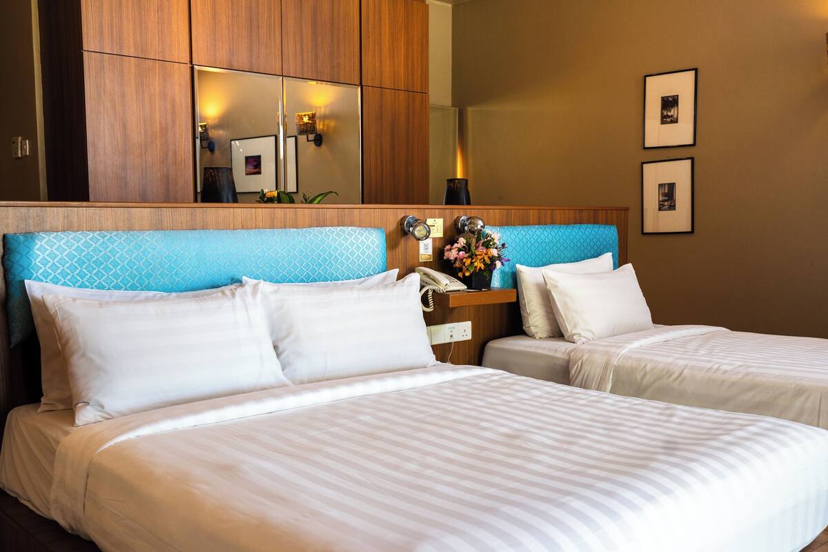 A hotel room with two beds, a wooden headboard, a nightstand with a lamp, and framed pictures on the wall.