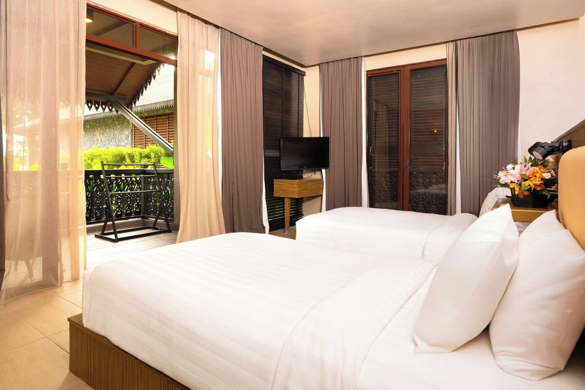 A hotel room with a large bed, a TV, and a balcony with a view of greenery.
