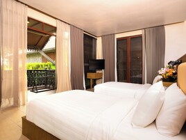 Quarto de hotel com uma cama grande, televisão e varanda com vista para vegetação.