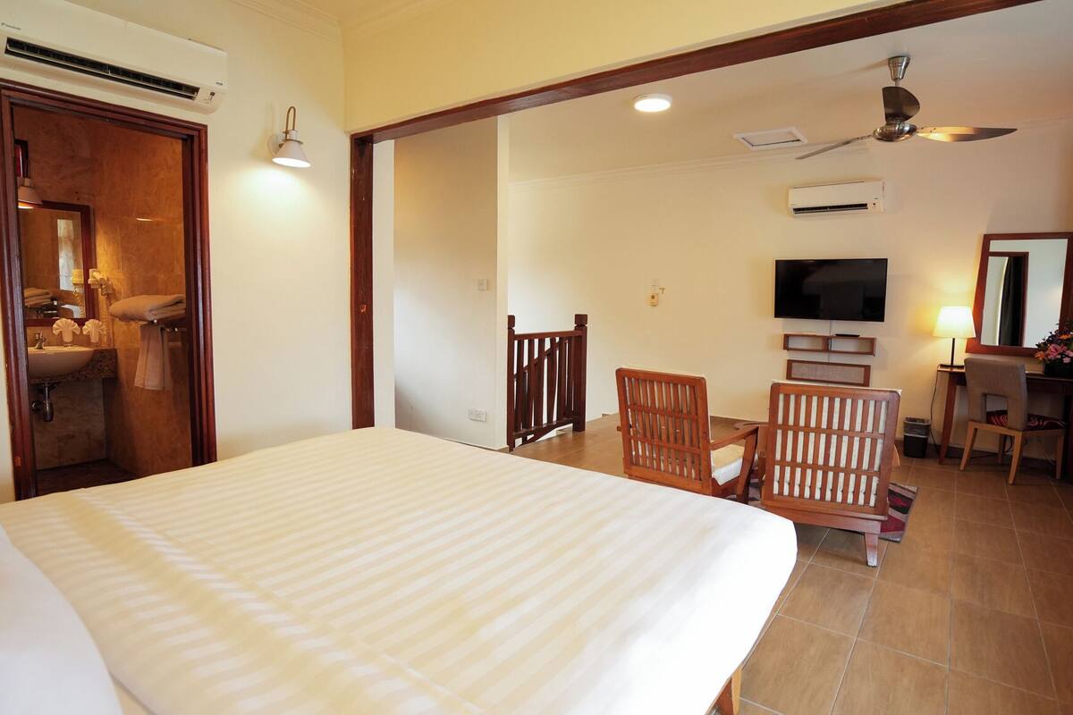 A hotel room with a bed, a desk with a chair, a TV, and a ceiling fan.