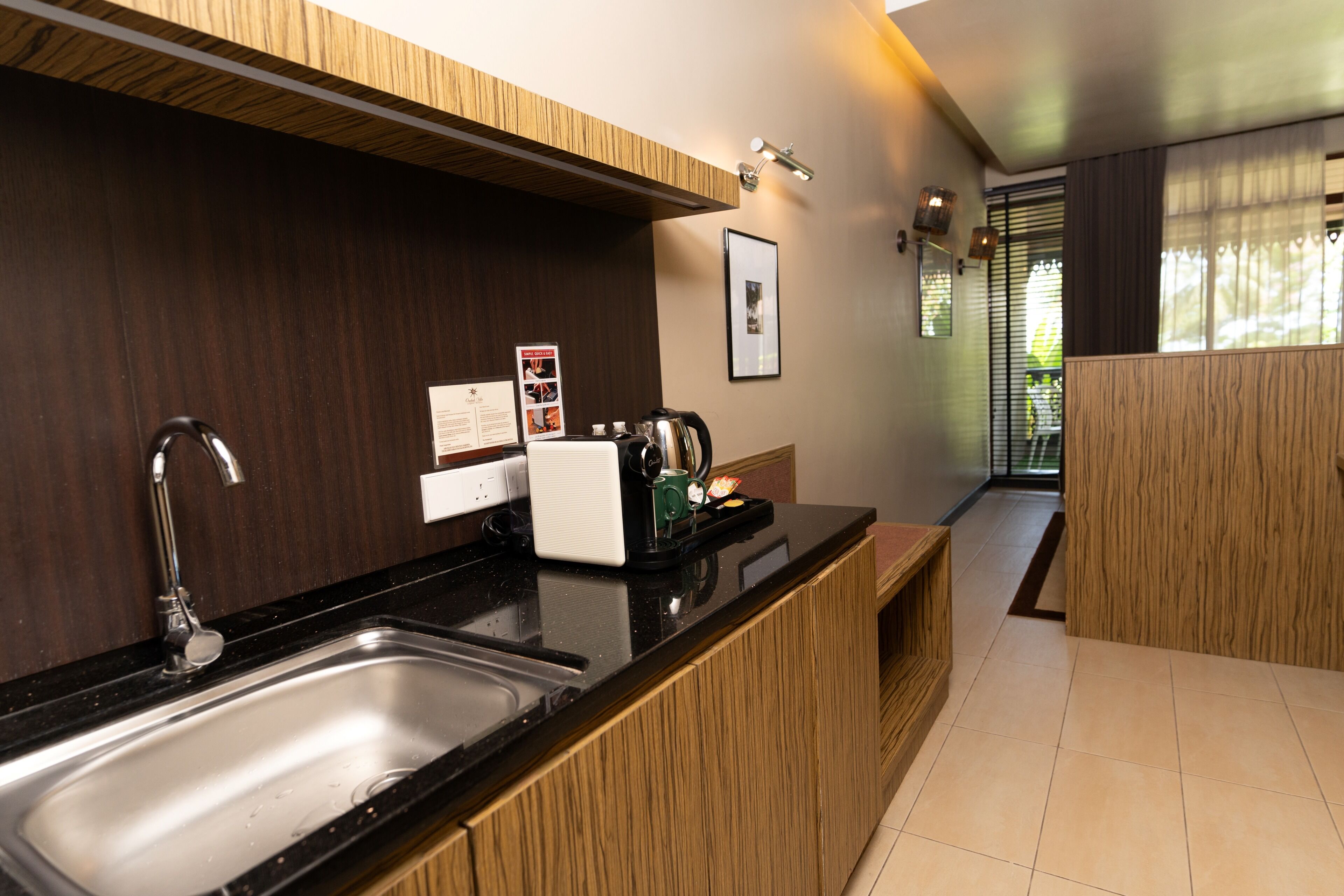 A modern kitchen with a stainless steel sink, wooden cabinets, a coffee machine, and a framed picture on the wall.