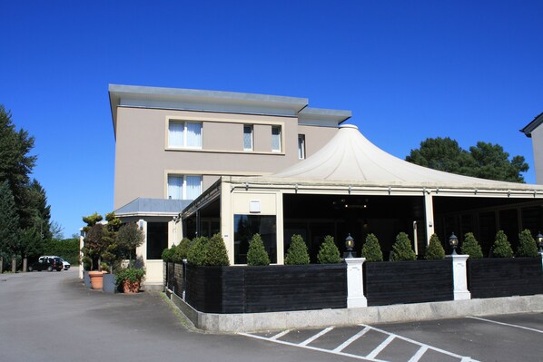 A modern building with a covered outdoor area, a parking lot, and a clear blue sky.