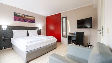 A hotel room with a bed, a desk, a chair, a TV, and a red door.