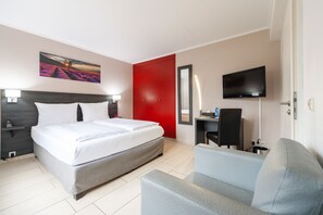 A hotel room with a bed, a desk, a chair, a TV, and a red door.