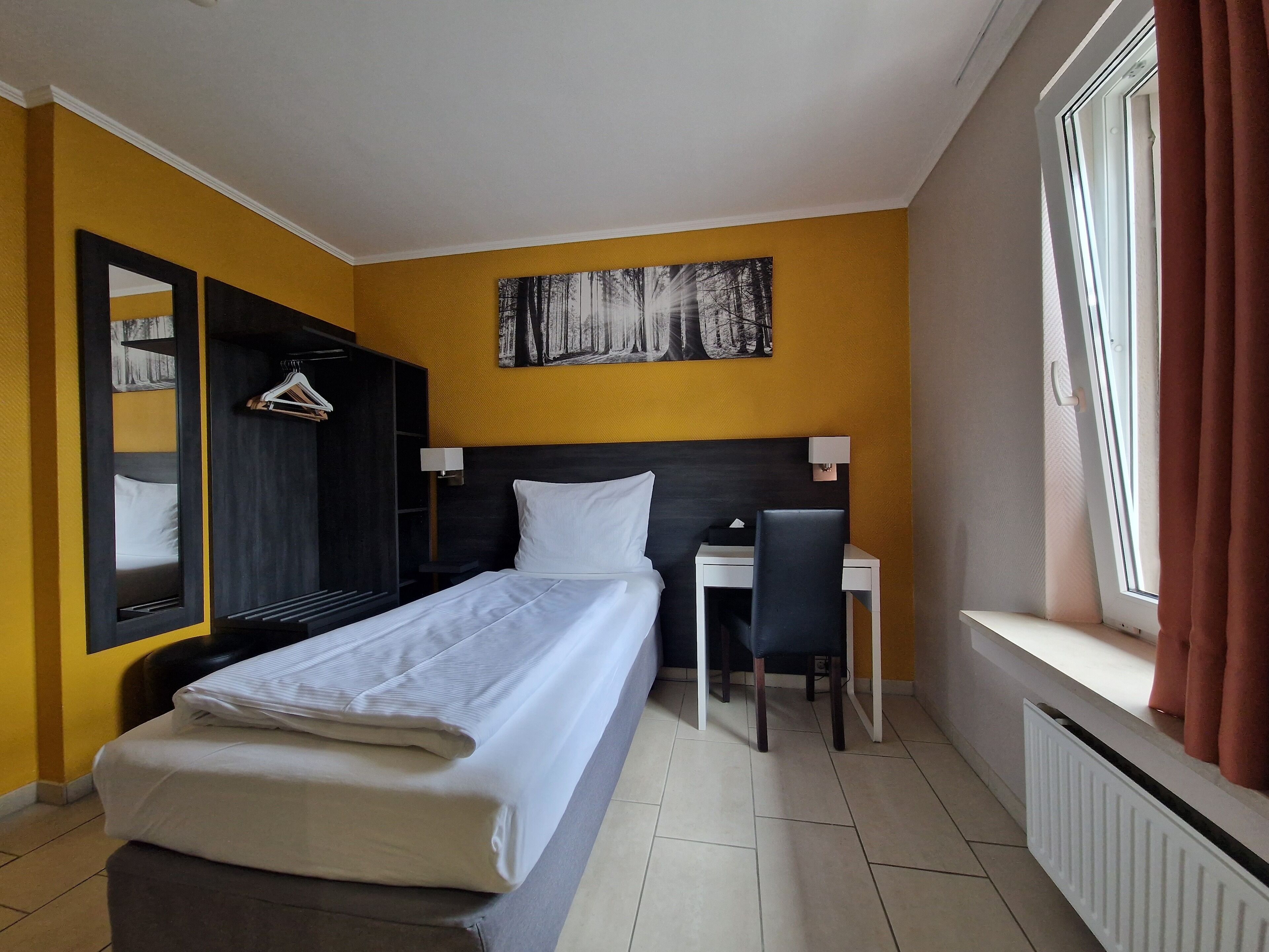 A hotel room with a bed, a desk, a chair, a wardrobe, and a window with curtains.
