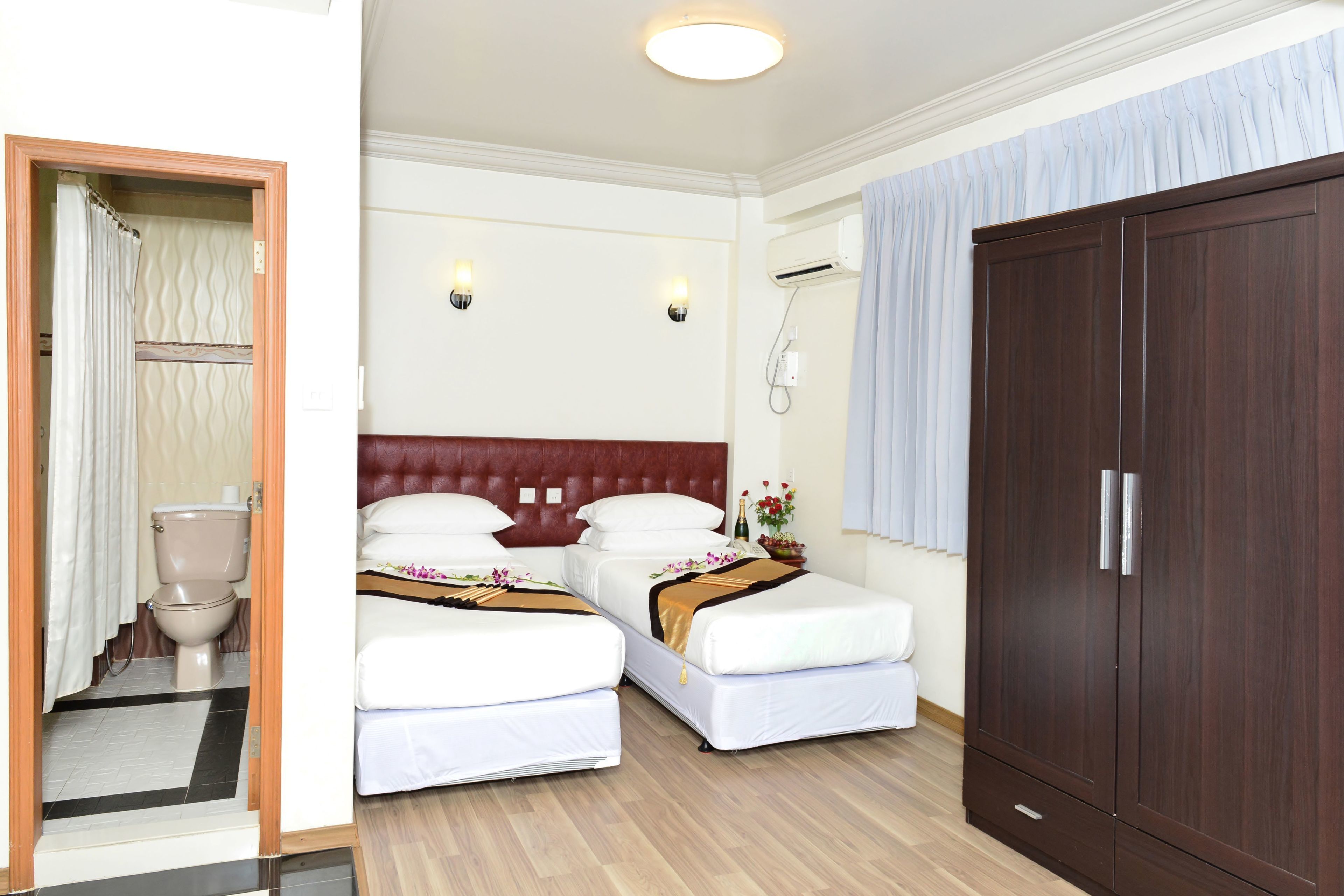 Een hotelkamer met twee bedden, een houten garderobe, een douche en een toilet.