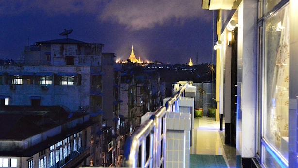 Ein Balkon mit Blick auf eine beleuchtete Stadtlandschaft bei Nacht, darunter Gebäude und ein weit entferntes Tempelgebäude.