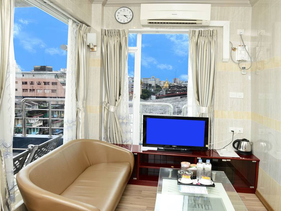 Habitación de hotel con un ventanal grande, un sofá, un televisor de pantalla plana y una cafetera sobre una mesita.