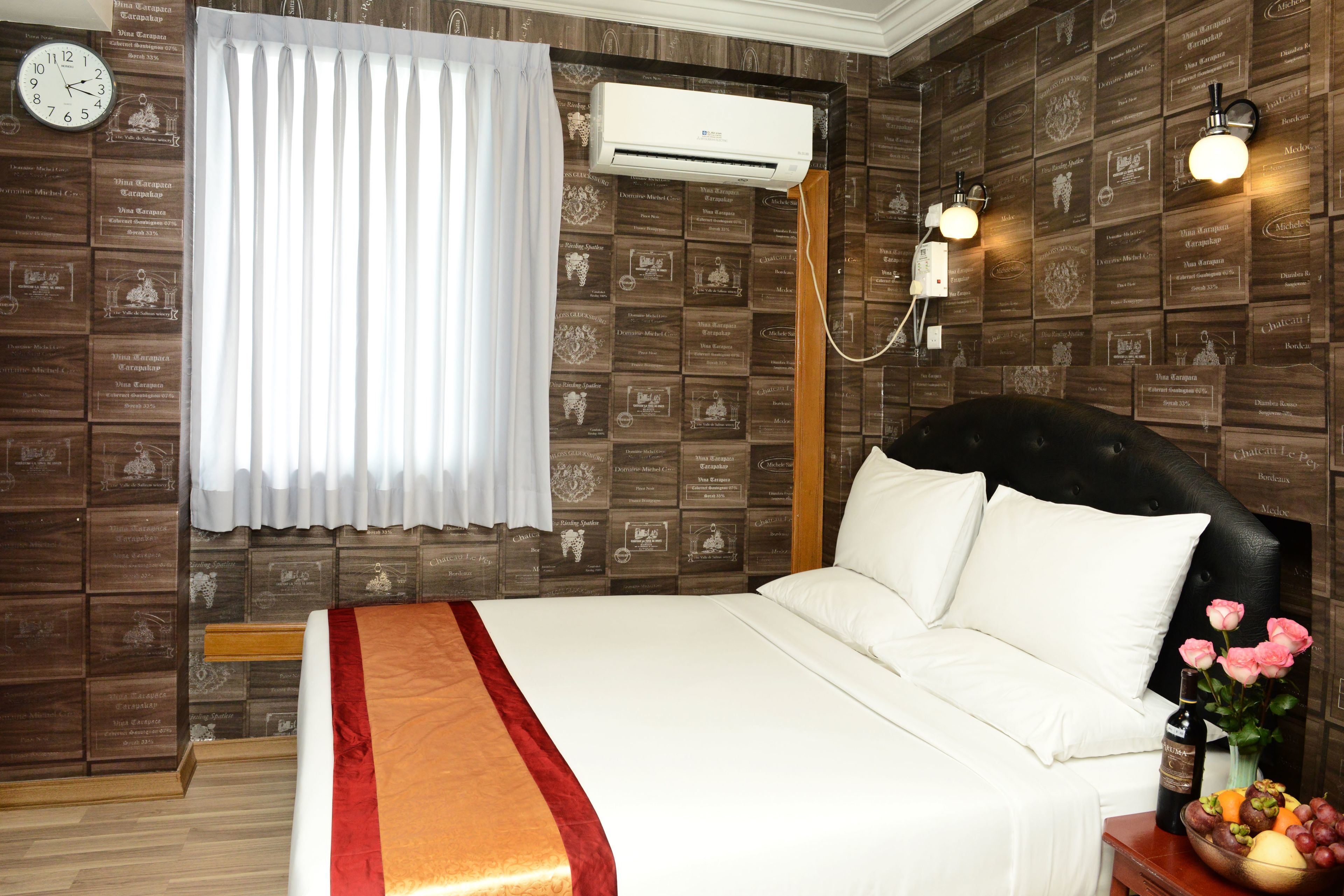 Una habitación de hotel con cama, un reloj, aire acondicionado y una pared con placas.