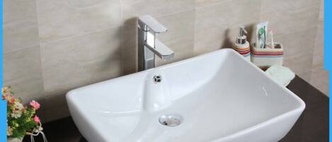 A modern bathroom with a white sink, chrome faucet, and a small soap dispenser.