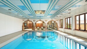 An indoor swimming pool with clear blue water, surrounded by arched doorways and large windows.