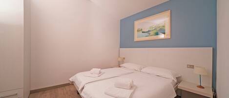 A hotel room with two beds, a painting on the wall, and a desk with a lamp.