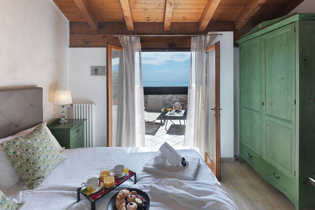 A bedroom with a bed, a bedside table, a green wardrobe, and a view of the sea through a door.