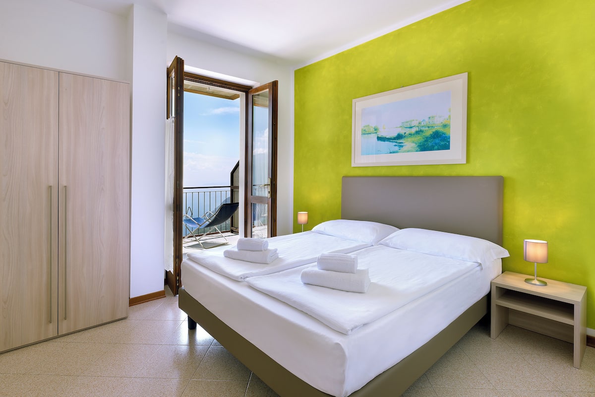A hotel room with a bed, a nightstand, a chair by the window, and a balcony.