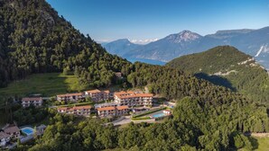 A hillside hotel with multiple buildings, a swimming pool, and a view of mountains and a lake.
