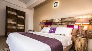 A neatly made bed with a white and purple bedspread, a wooden headboard, and a nightstand with a lamp. - The Swiss Hotel (Freetown)