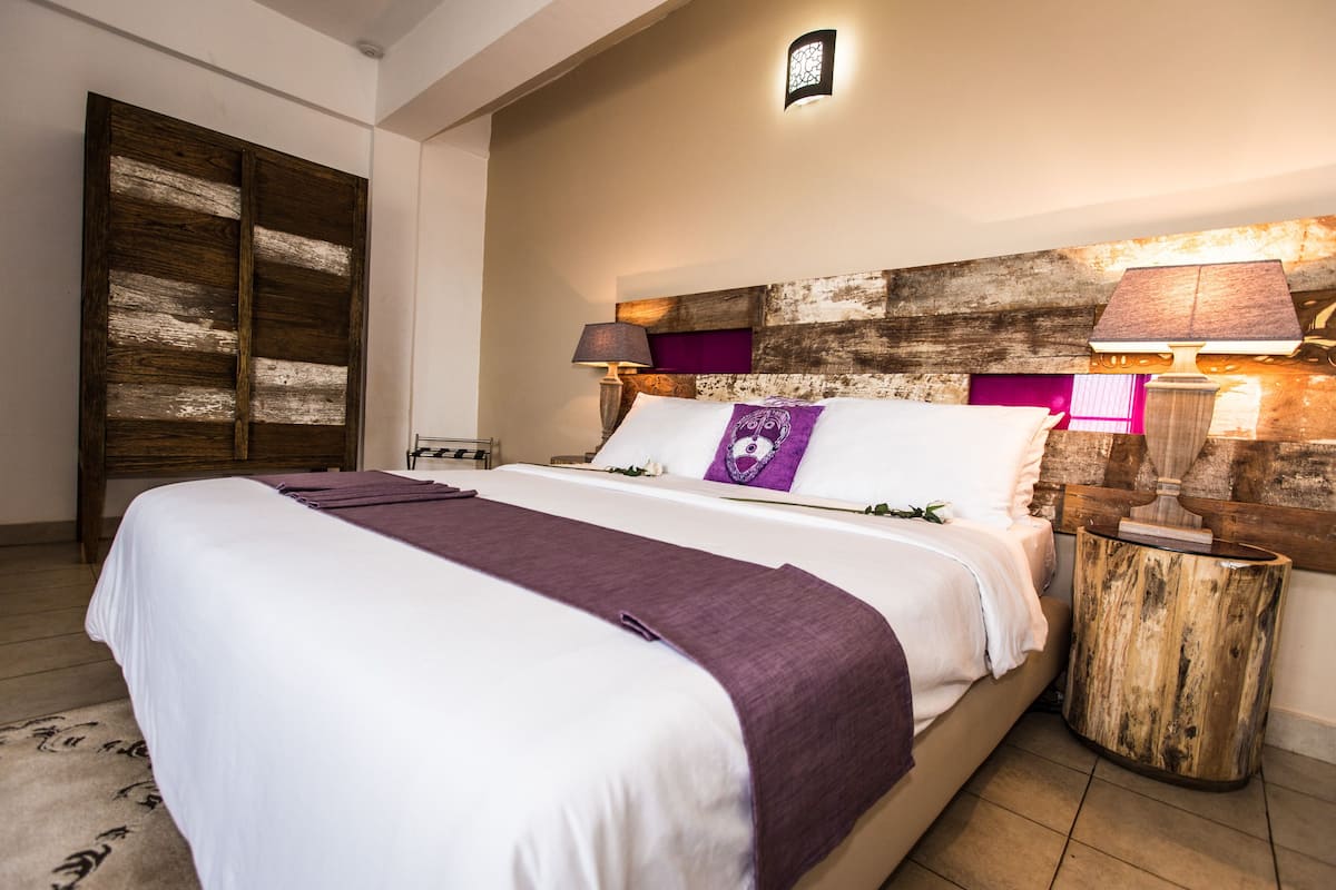 A neatly made bed with a white and purple bedspread, a wooden headboard, and a nightstand with a lamp.