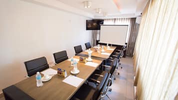 A conference room with a long table, chairs, a projector screen, and a television.