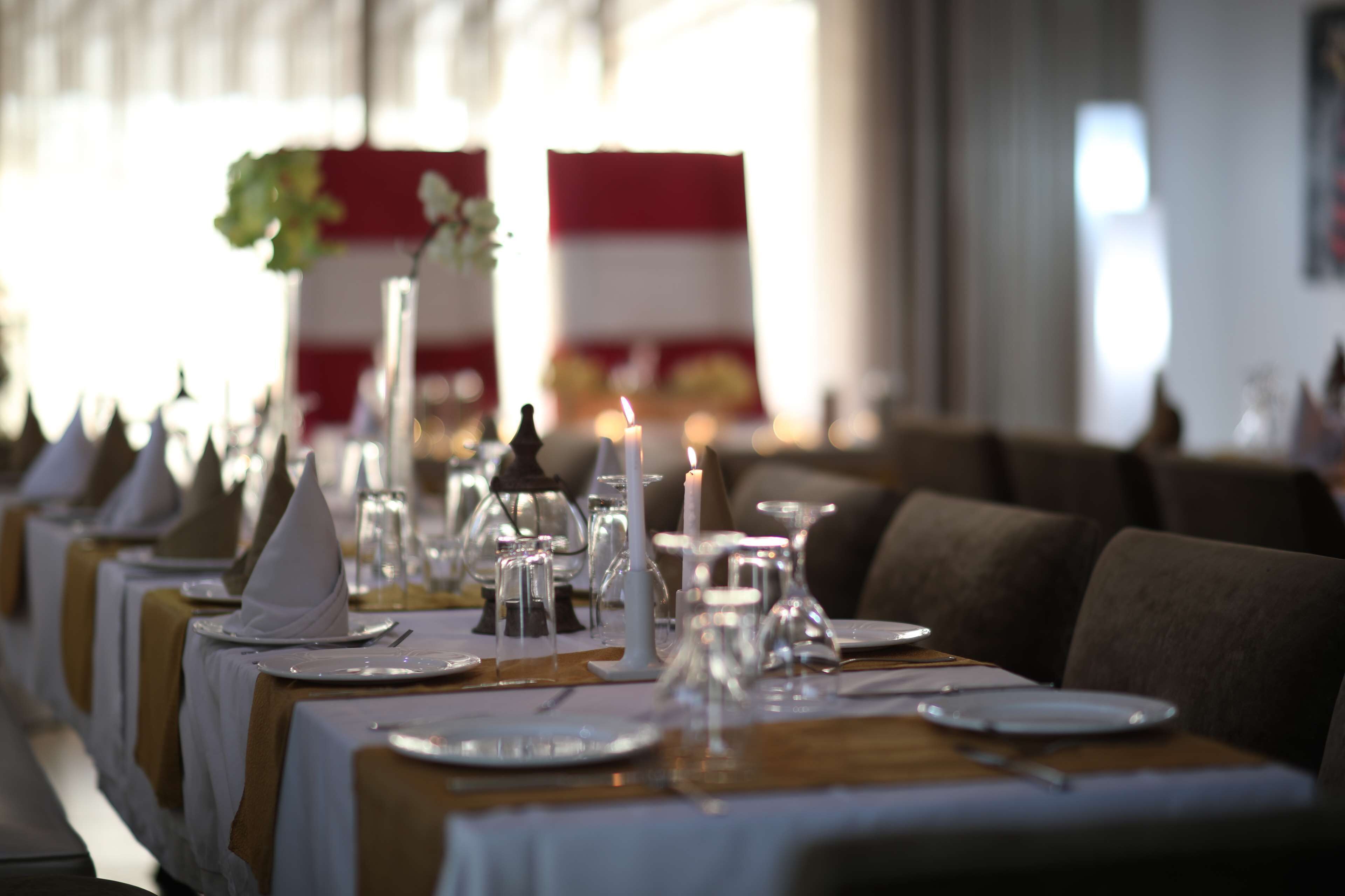 A long dining table set with white napkins, plates, and glassware, with candles and a flower centerpiece.