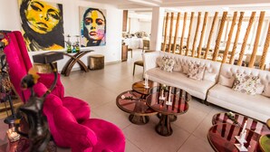 A modern living room with a white sofa, round glass coffee tables, and vibrant artwork on the walls. - The Swiss Hotel (Freetown)