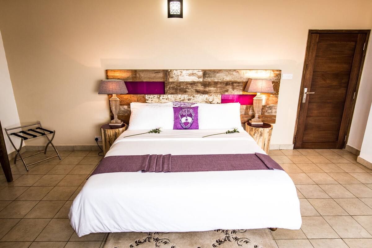 A neatly made bed with a white and purple bedspread, two bedside lamps, and a wooden headboard.