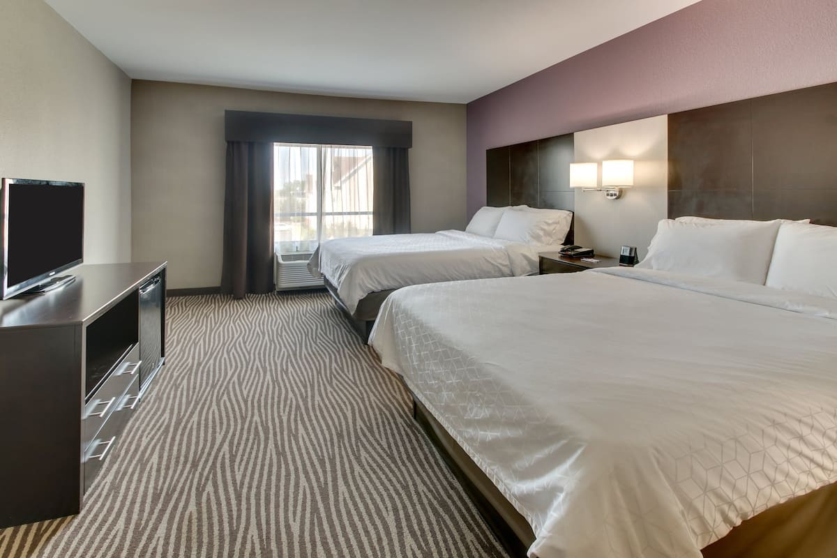 A hotel room with two beds, a TV, a desk, and a window with curtains.