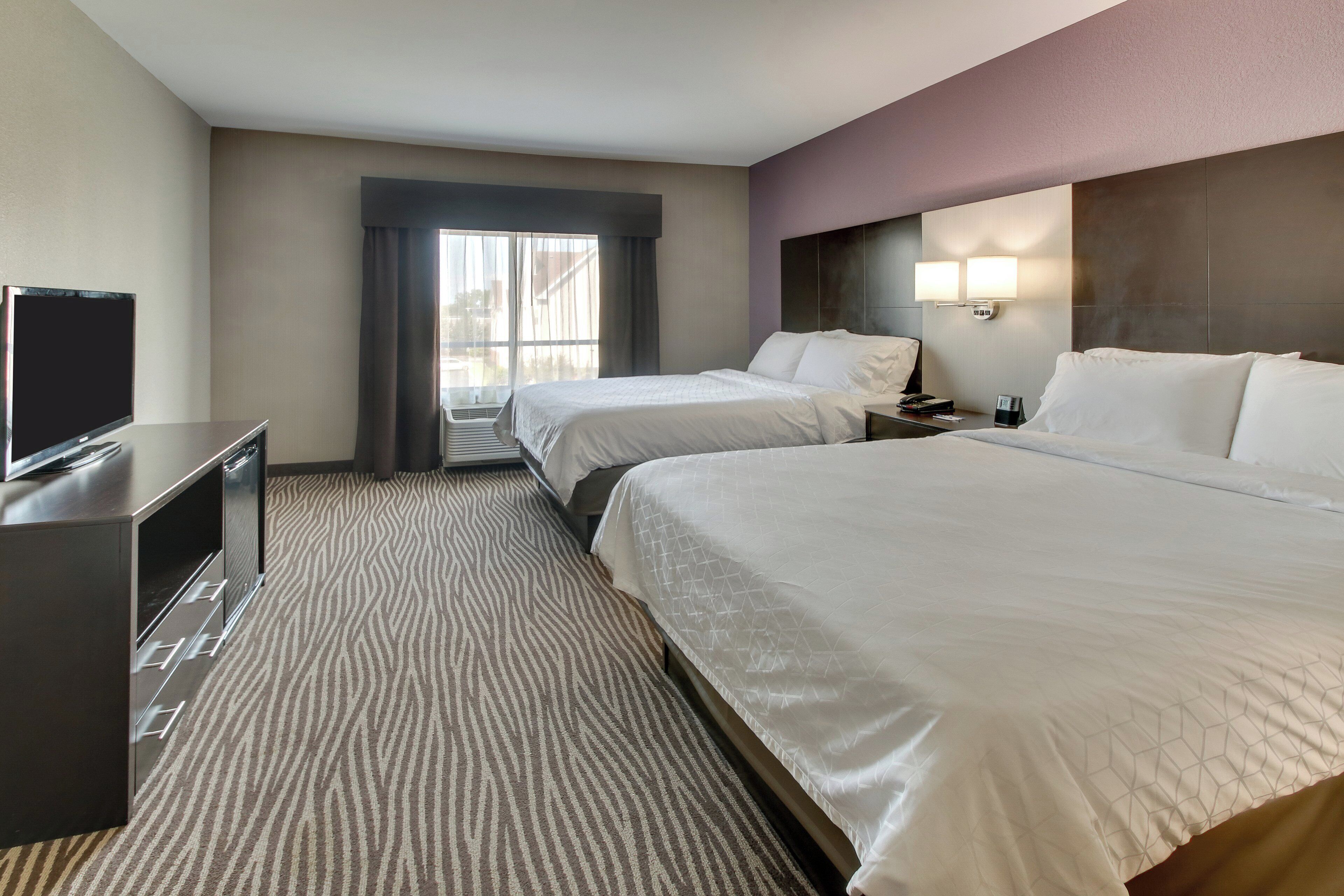 Quarto de hotel com duas camas, televisão, secretária e janela com cortinas.