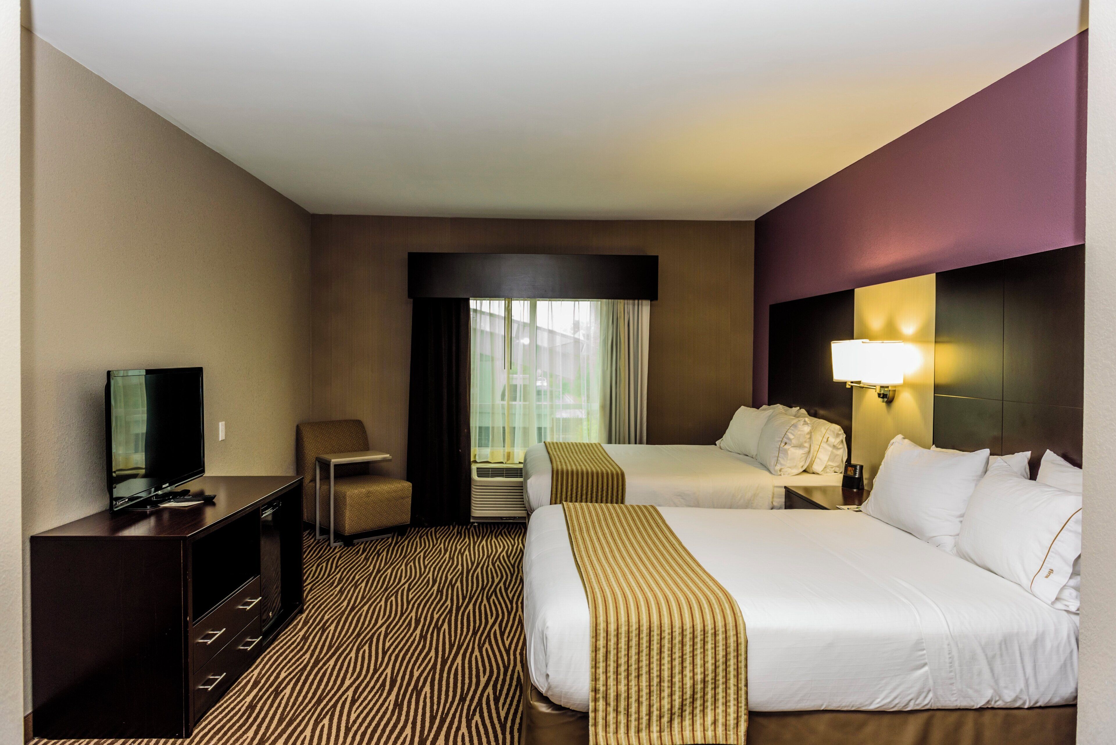 A hotel room with two beds, a TV, a desk, and a chair.
