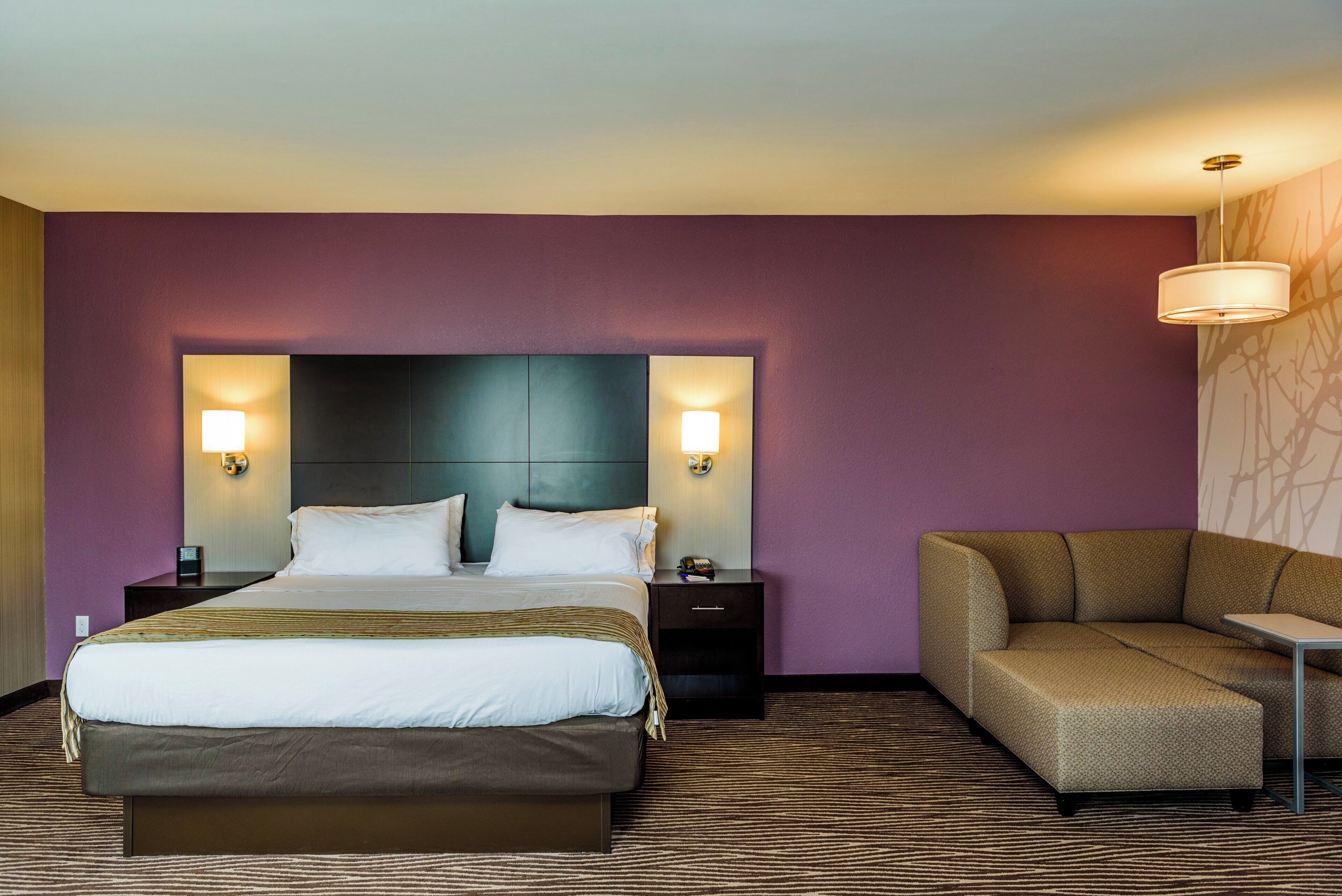 A hotel room with a large bed, two bedside tables, a sofa, and a wall-mounted lamp.