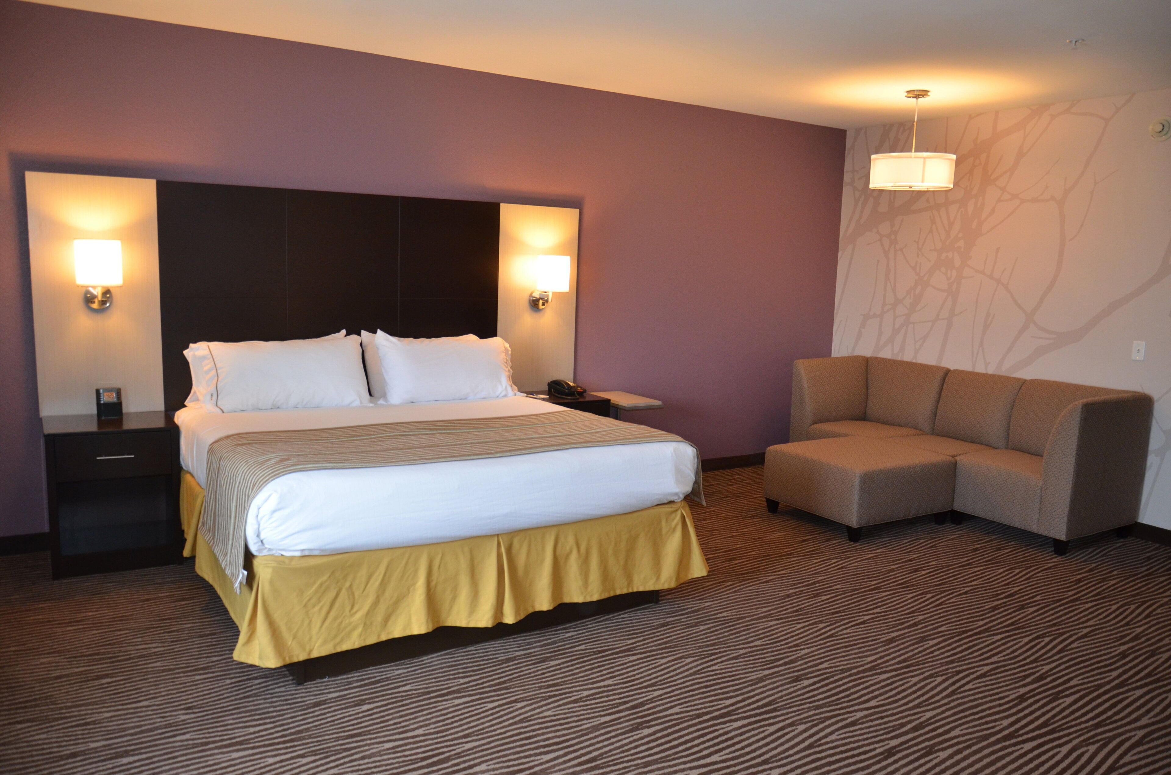 A hotel room with a bed, bedside tables, a sofa, and wall-mounted lamps.