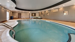 Una amplia piscina cubierta de borde curvo, un área de descanso con sofás y una puerta que da a otra habitación.