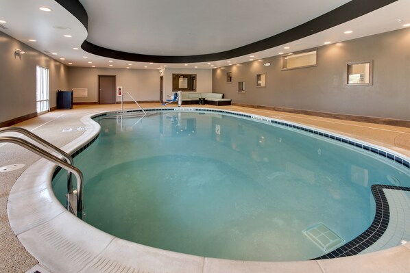 A large indoor swimming pool with a curved edge, a lounge area with a sofa, and a door leading to another room. - Holiday Inn Express Cheektowaga North East by IHG (Buffalo)