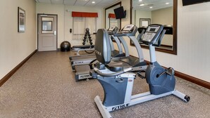 Un gimnasio con cintas de correr, una bicicleta estática y un banco para pesas.