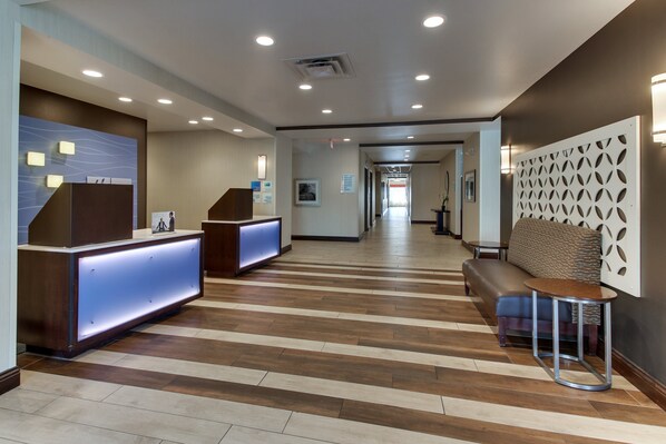 A hotel lobby with a reception desk, seating area, and a long corridor. - Holiday Inn Express Cheektowaga North East by IHG (Buffalo)