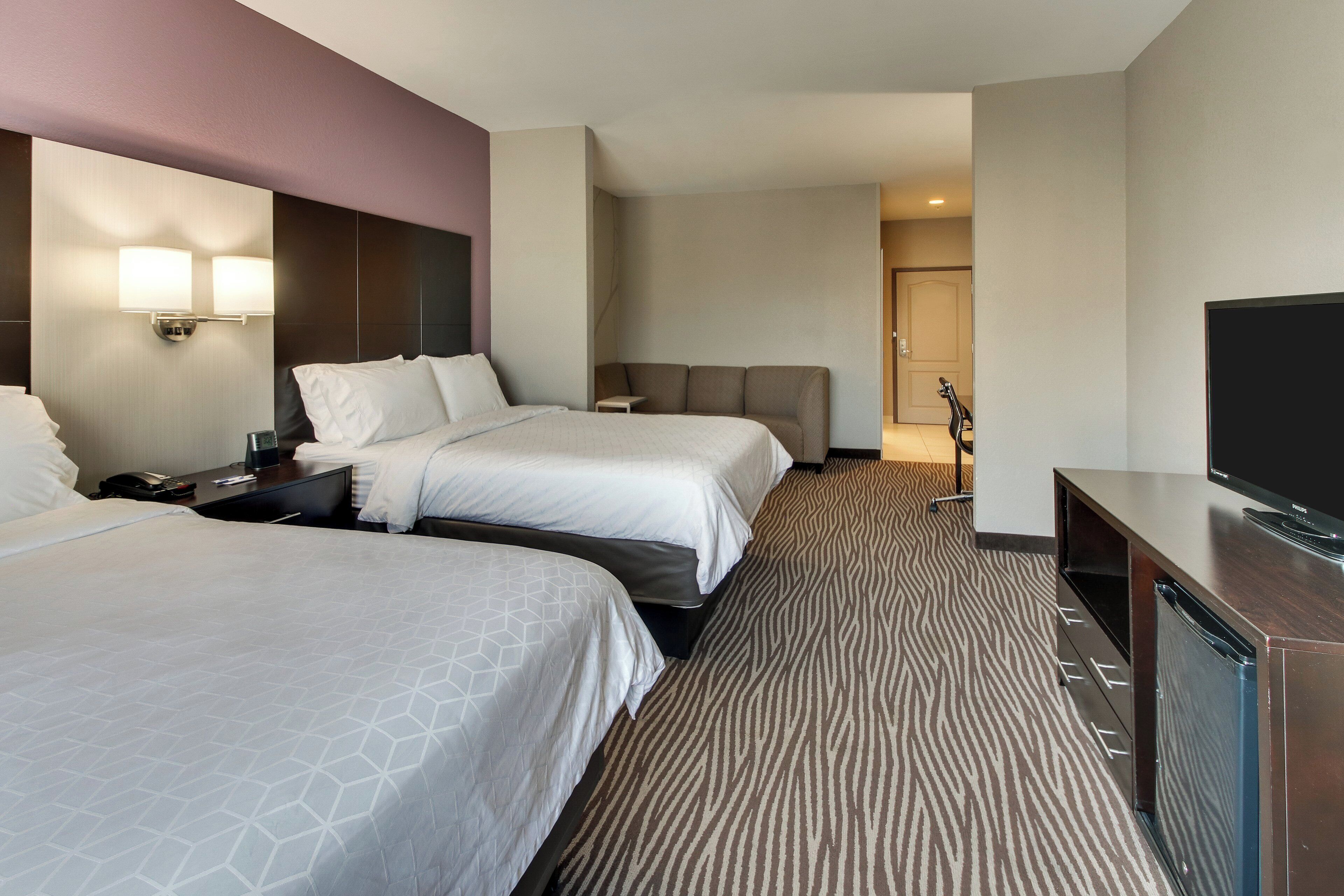 A hotel room with two beds, a flat-screen TV, a desk, and a patterned carpet.