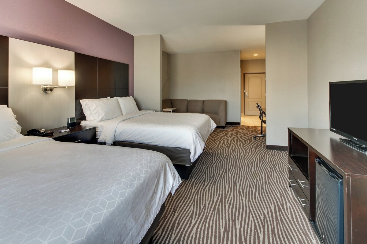 A hotel room with two beds, a flat-screen TV, a desk, and a patterned carpet.