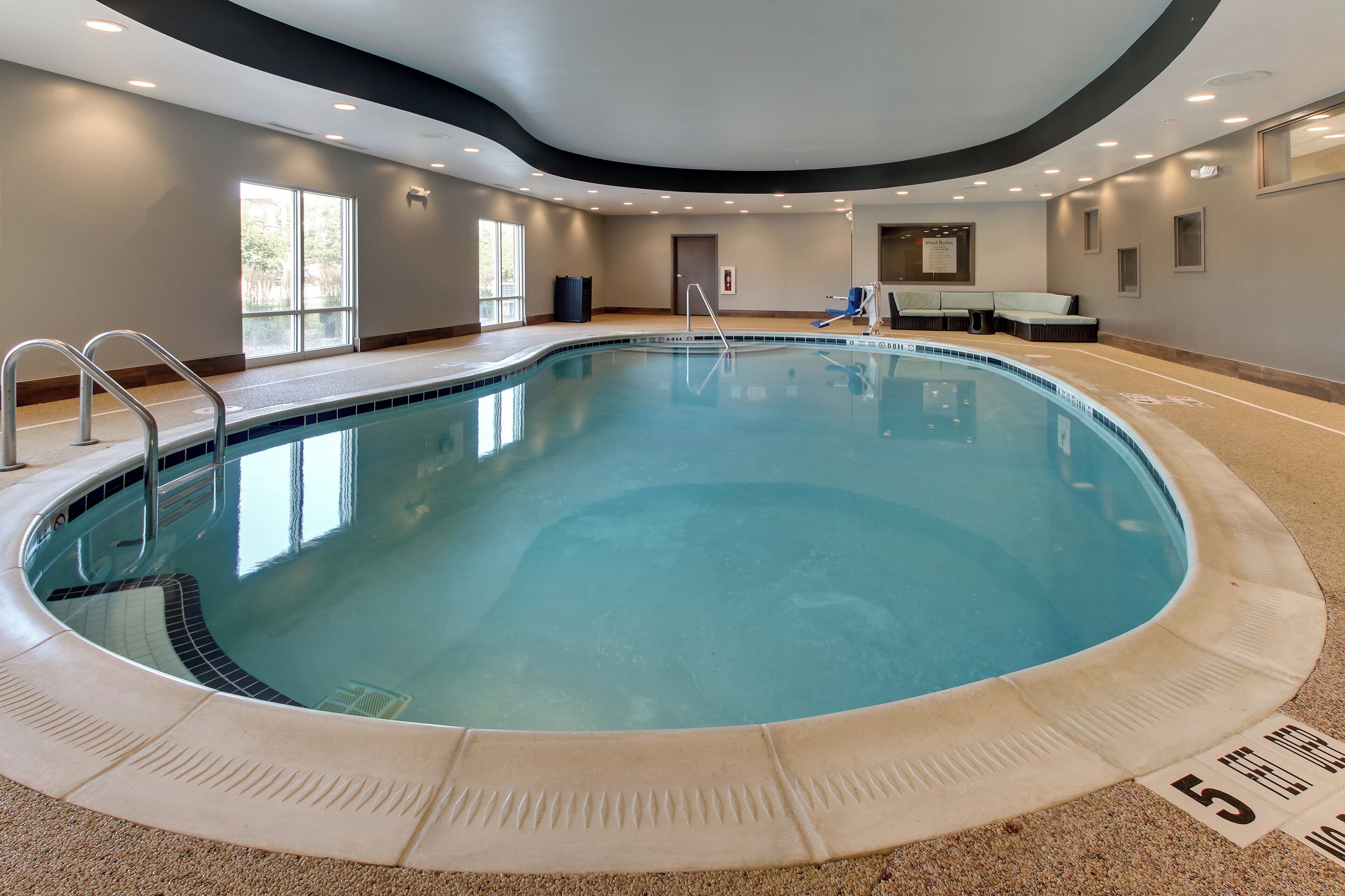 A large indoor swimming pool with a clear blue water surface, surrounded by a tiled deck and a low wall.