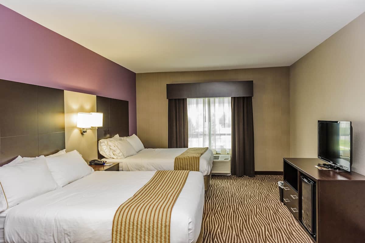 A hotel room with two beds, a television, a desk, and a window with curtains.