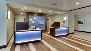 A hotel reception area with a modern design, featuring a reception desk, a digital display, and a framed picture on the wall. - Holiday Inn Express Cheektowaga North East by IHG (Buffalo)