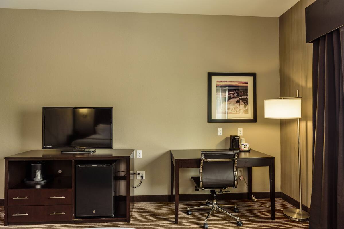 A hotel room with a TV, a desk with a chair, a lamp, and a small refrigerator.