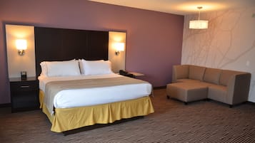 A hotel room with a large bed, bedside tables, a sofa, and a wall-mounted lamp.