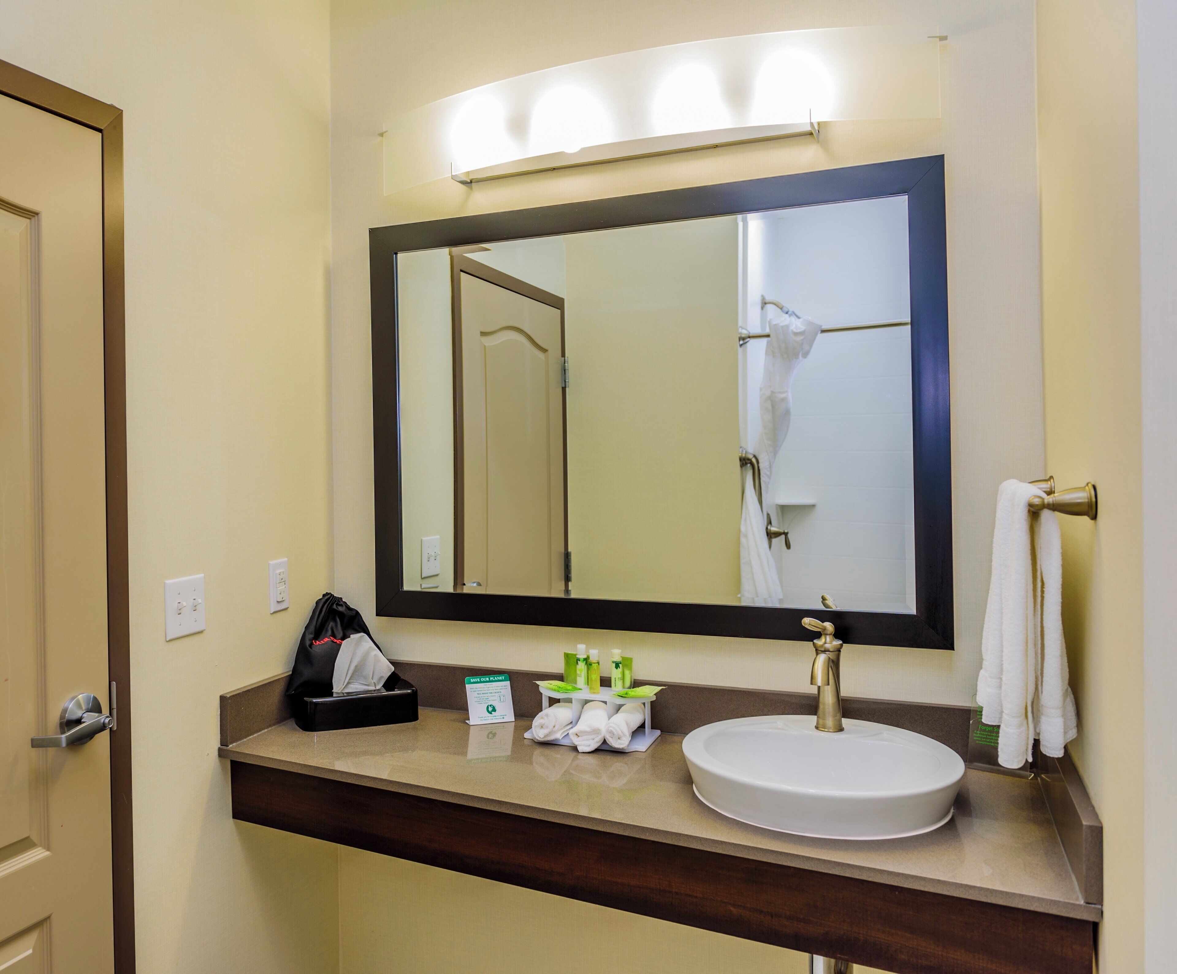 A bathroom with a sink, mirror, towel rack, and a sign indicating a green initiative.