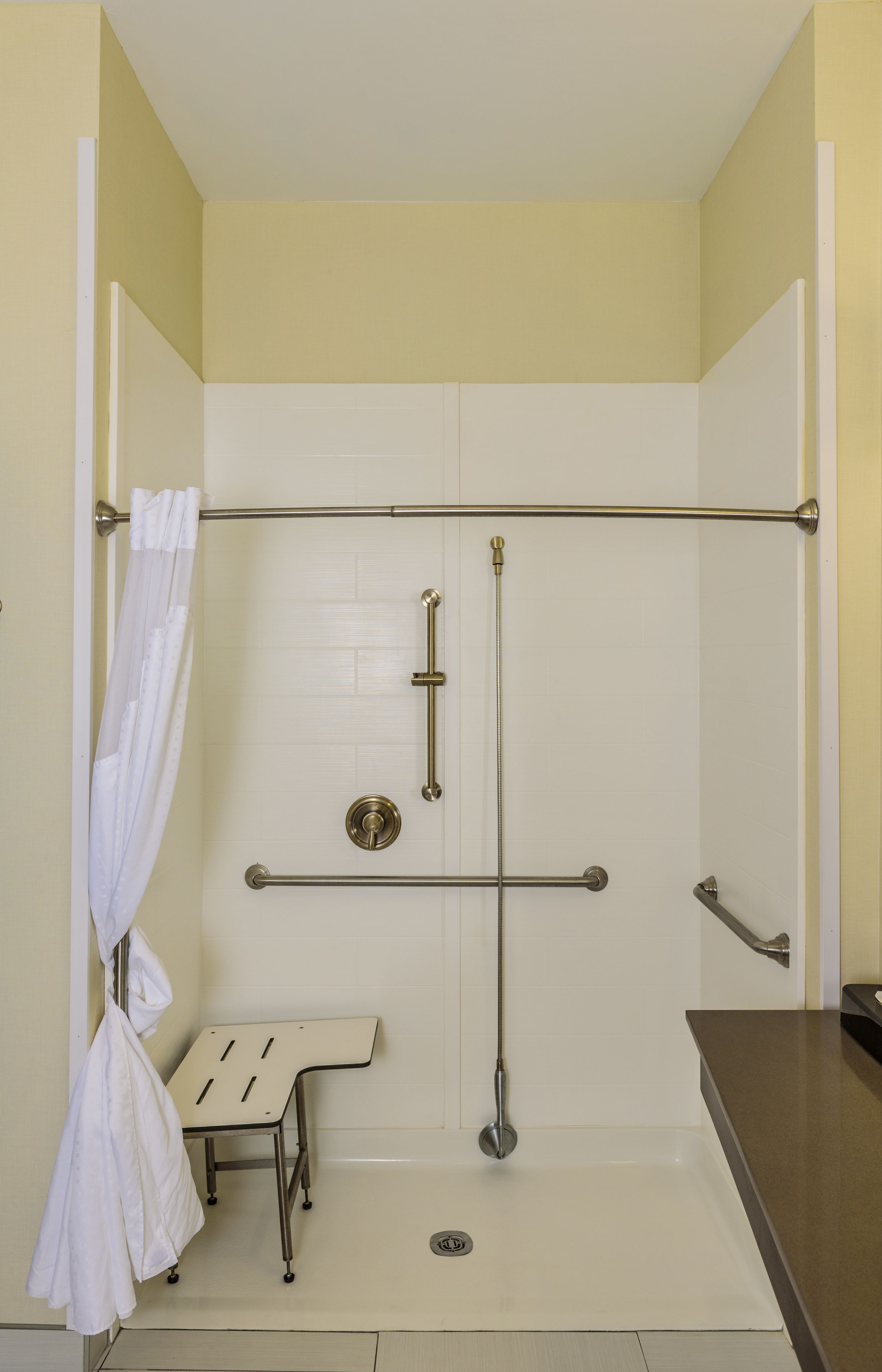 A bathroom with a shower area, a grab bar, a bench, and a towel rack.