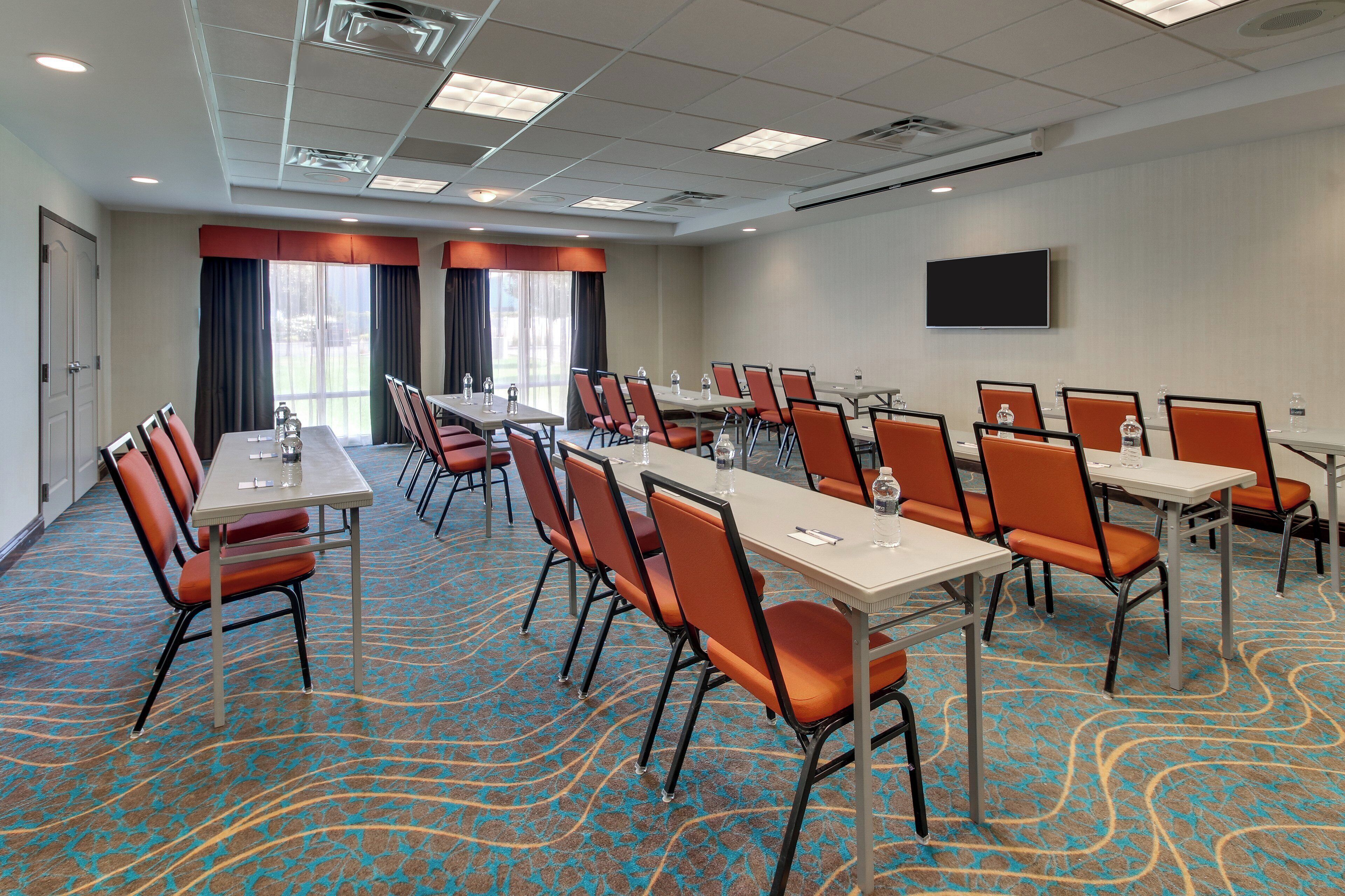 A conference room with tables and chairs, a flat-screen TV, and a patterned carpet.