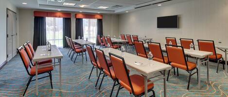 A conference room with tables and chairs, a flat-screen TV, and a patterned carpet.