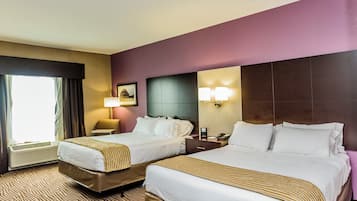 A hotel room with two beds, a large window with curtains, a wall-mounted lamp, and a framed picture.