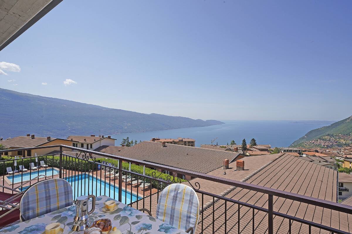 A balcony with a pool, a table with chairs, and a view of the sea and mountains.